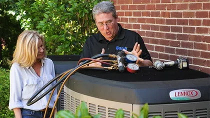 Technician explaining air conditioning unit features to a homeowner outdoors.