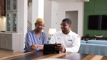Technician in Bardi uniform consulting with woman in modern home using a tablet at dining table.