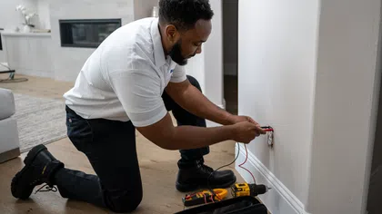 Electrician kneeling on floor fixing outlet wiring in a modern home with tools on wooden floor