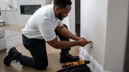 Electrician kneeling on floor fixing outlet wiring in a modern home with tools on wooden floor