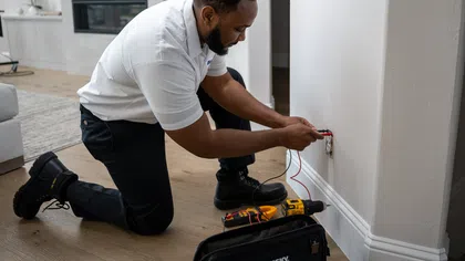 Electrician kneeling on floor fixing outlet wiring in a modern home with tools on wooden floor