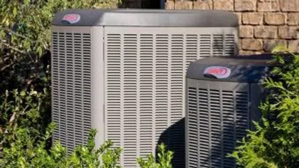 Two air conditioning units surrounded by greenery, showcasing outdoor cooling systems in residential area.