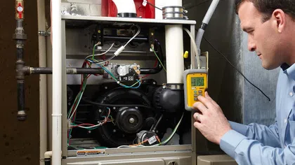 Technician inspecting a furnace with digital multimeter in a home setting.