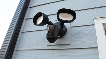 Smart security camera with dual floodlights mounted on exterior wall of a house.