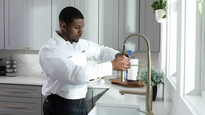 A technician adjusts a kitchen faucet in a modern, stylish kitchen with natural light.
