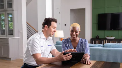 Technician and client reviewing plans on a tablet in a modern living room setting with natural light.