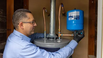 Technician installs a blue water heater expansion tank, demonstrating plumbing work.