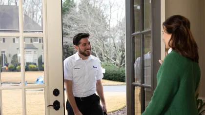 A friendly service technician greets a homeowner at the front door, showcasing professionalism and customer service.