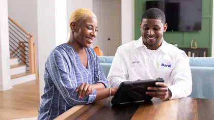 Smiling woman and technician engaged with a tablet at a modern table in a bright home interior.
