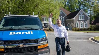 A technician waves goodbye while approaching a service van in a residential neighborhood.