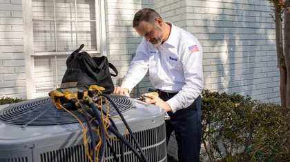 Technician servicing an outdoor air conditioning unit with tools, bright sunlight illuminating the scene.
