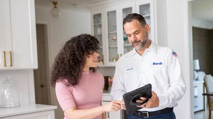 Service technician showing a tablet to a woman in a modern kitchen discussing appliance options.