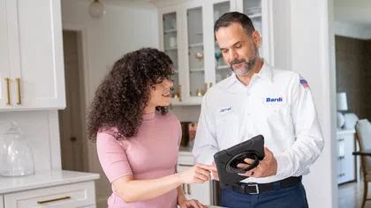 Service technician showing a tablet to a woman in a modern kitchen discussing appliance options.