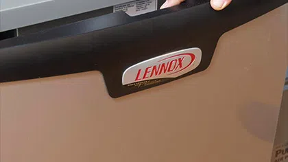 Close-up of a hand operating a Lennox HVAC unit, highlighting its modern design and control panel.
