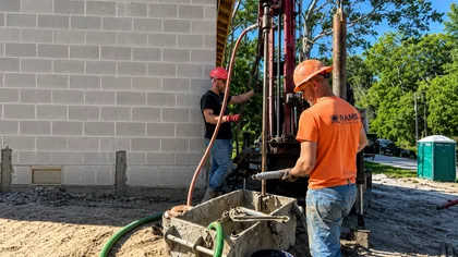 Construction workers operate drilling equipment for foundation work at a building site on a sunny day.