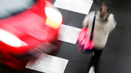 Blurred red car speeding past a pedestrian crossing with a person walking across a zebra crosswalk.