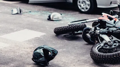 Fallen motorcycle and helmet on the road after a collision with a car in the background and shattered glass nearby.