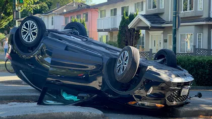 Black car overturned on a city street near a traffic light and residential buildings during daytime
