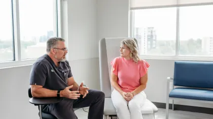 Doctor in black scrubs consulting female patient in pink top in a bright medical office with large windows.
