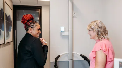 Two women smiling and talking in a modern office hallway with artwork on the walls.