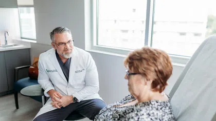 Doctor in white coat consulting with a seated female patient in a modern medical office with natural light.