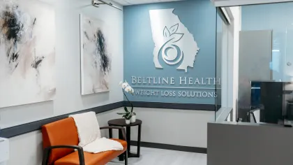 Modern waiting room with orange chair, abstract wall art, and Beltline Health Weight Loss Solutions logo on blue wall.