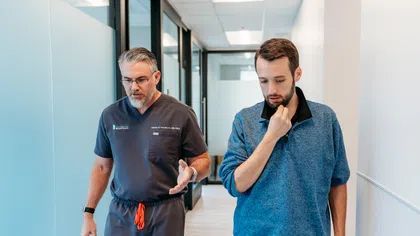 Doctor in scrubs discussing with a patient walking down a medical office hallway