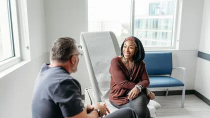 Smiling woman talking with male doctor in modern medical office with natural light and city view windows