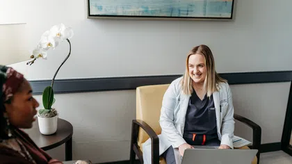 Female doctor with laptop smiling and consulting a patient in a modern medical office with orchid plant.
