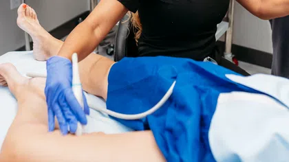 Healthcare professional performing ultrasound therapy on patient's leg in clinical setting with medical equipment.