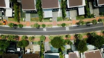 Aerial view of suburban street with modern houses, greenery, sidewalks, and a parked orange car.