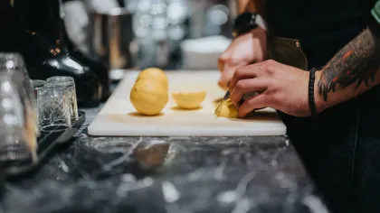 Person with tattooed arm slicing lemons on a white cutting board in a kitchen setting