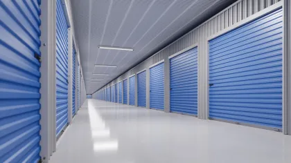 Indoor storage facility corridor with rows of blue roll-up doors and bright overhead lighting