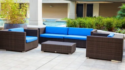 Outdoor patio furniture set with blue cushions and brown wicker frame on tiled floor near greenery