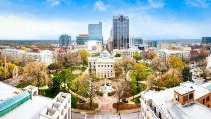Aerial view of a city park with historic buildings, tall skyscrapers, and autumn trees under a blue sky.
