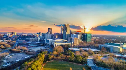 Aerial view of a city skyline at sunset with colorful sky and urban greenery in foreground.