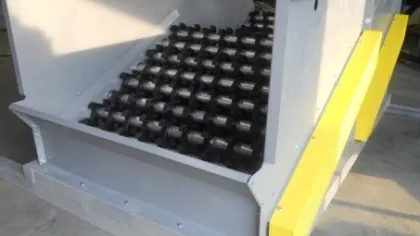 Industrial machine with black cylindrical rollers arranged on a sloped gray and yellow metal frame.