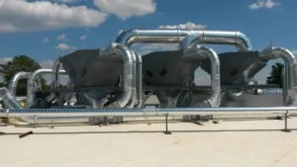 Large industrial ventilation system with metal ductwork and funnels on a rooftop under a blue sky.