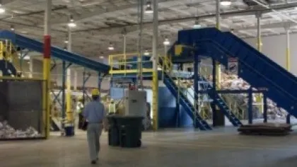 Worker walking inside a large recycling facility with conveyor belts and machinery sorting materials
