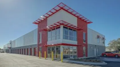 Modern red and gray commercial building with large windows and clear blue sky on a sunny day