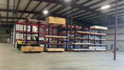 Warehouse interior with metal racks storing wooden pallets and building materials under industrial lighting.