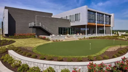 Modern building with an outdoor putting green, landscaped garden beds, and blue sky background