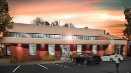 Modern single-story brick office building with large windows and parked cars at sunset under colorful sky
