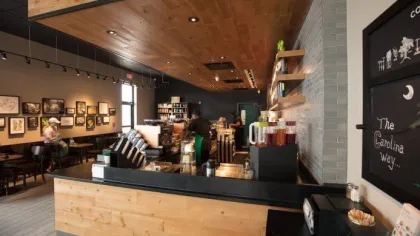 Cozy coffee shop interior with wooden counter, shelves, framed artwork, and customers sitting and ordering.