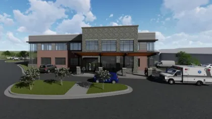 Modern two-story medical facility with ambulance, cars, landscaped entrance, and clear sky background.