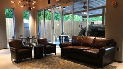 Cozy lounge area with brown leather sofa, armchairs, patterned rug, modern lighting, and glass sliding doors opening outdoors.