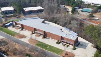 Aerial view of a large brick commercial building surrounded by parking and trees in a suburban area.