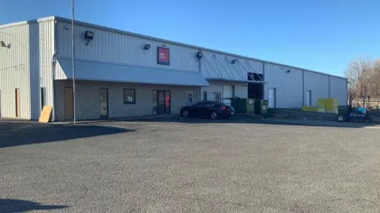 Large industrial warehouse with metal siding, multiple doors, a parked black car, and a clear sky above.