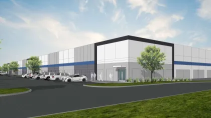 Modern industrial warehouse with parked cars, trees, and a blue stripe accent under a partly cloudy sky.