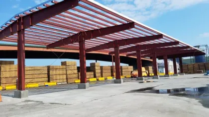 Steel framework construction at a lumber yard with stacked wood and clear blue sky overhead